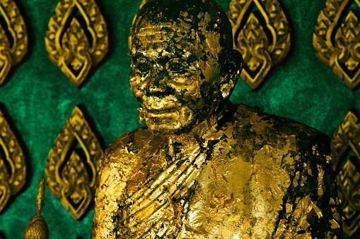 Close-up shot of a shabby praying buddhist monk statue covered in golden paint.