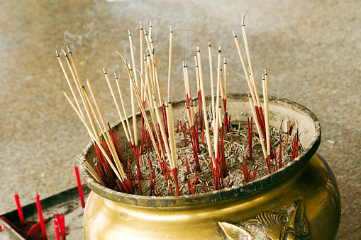 Closeup shot of an old traditional censer filled with smoldering sticks inside a buddhist temple.