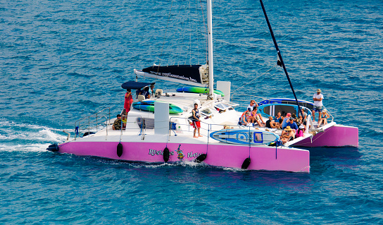 Royal Naval Dockyard, Bermuda-May 23, 2022- A group of smiling passengers relax on the front net of the pink catamaran tour boat \