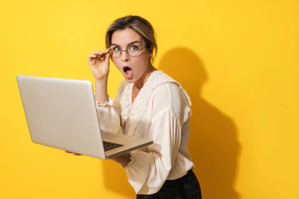 istock Suprised woman wearing eyeglasses using laptop computer on yellow background 1403535363