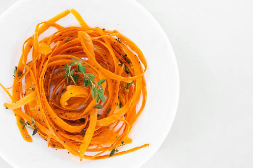 Photo of vibrant orange noodles made from carrots, as a low-carb and vegan alternative to traditional pasta. Shot from above in a white bowl with clean white background.