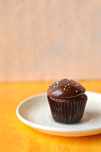 Mini Nutella cupcakes topped with chocolate ganache and Nutella. Sprinkled with some funfetti. Captured on orange background.
