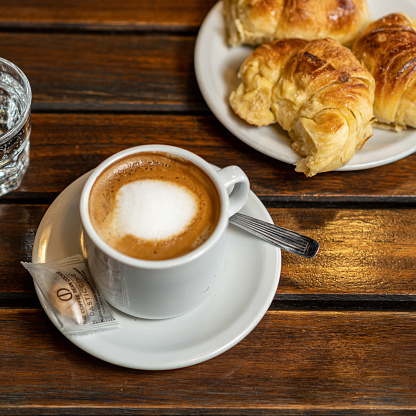 a served breakfast, with a cup of coffee and some croissants, on a wooden table.