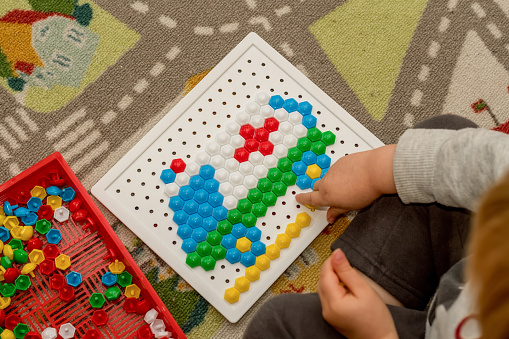 Toddler playing pegboard mosaic. Early child development. Fine motor skills. Learning and creativity