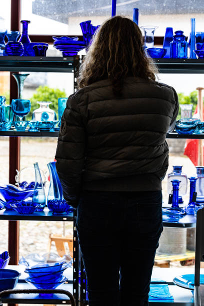 Hjorring, Denmark Hjorring, Denmark A woman window shopping for blue glassware in a vintage shop. hjorring stock pictures, royalty-free photos & images