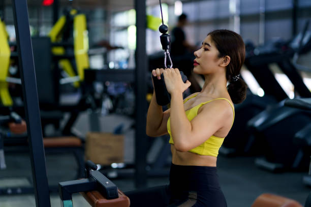 Young Asian woman flexing arm muscles on cable machine at gym. stock photo