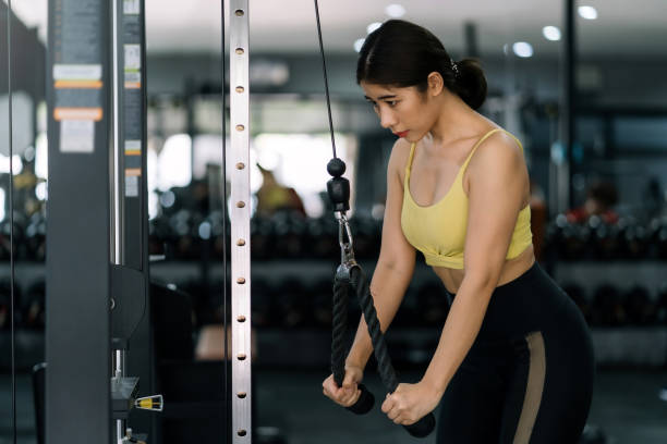 istock Young Asian woman flexing arm muscles on cable machine at gym. 1403575210