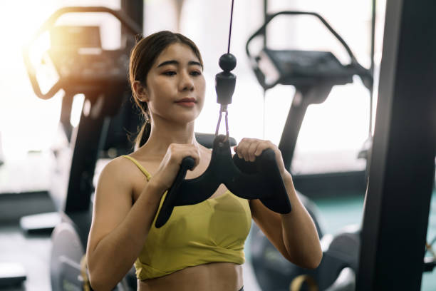 istock Young Asian woman flexing arm muscles on cable machine at gym. 1403575213