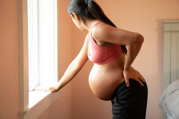 молодая беременная испаноязычная женщина готовится к родам через окно - bending over стоковые фото и изображения