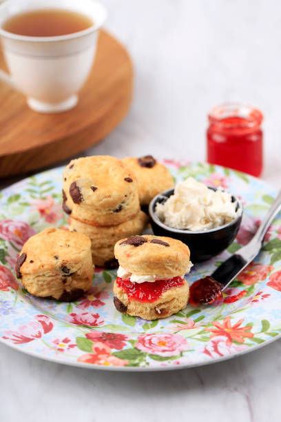 scones on a flowery plate, a jar of strawberry jam and a cup of tea - brownie tea afternoon tea scone imagens e fotografias de stock