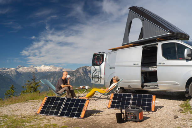 Self supporter mature couple on camping vacations in the mountains enjoying breakfast Sporty middle age couple sitting high up in the mountains, dachstein mountain glacier in background, beside their camper van with rooftop tent enjoying breakfast on sunny morning, self sufficient with portable solar panels, part of a series of camping travel camping solar panels stock pictures, royalty-free photos & images