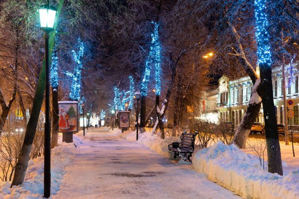 Ulyanovsk, Russia - February 14, 2022: Evening winter alley with benches and New Year's decorations. Snow-covered street in Christmas decorations.