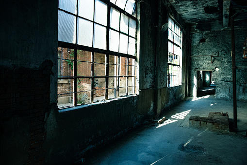 Viewing in an old room with big windows. Empty place in an abandoned building. Bricks come through the wall plaster and paint is peeling off. Ruined apartment in bad condition.