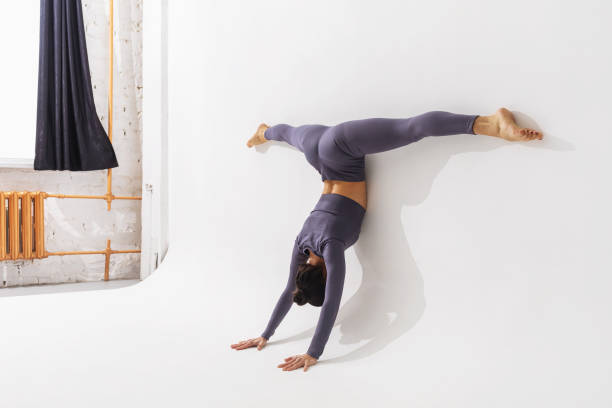 istock Woman practicing yoga, performs the Adho Mukha Vrikshasana exercise with Samakonasana, stands on her hands with a transverse twine, leaning her body against the wall 1403602733