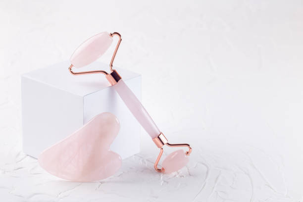 istock Rose quartz crystal facial roller and massage tool Gua sha with podium on white background, 1403603200