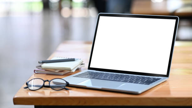 istock Computer laptop with white empty display, eyeglasses and notebooks on wooden office desk. 1403603249
