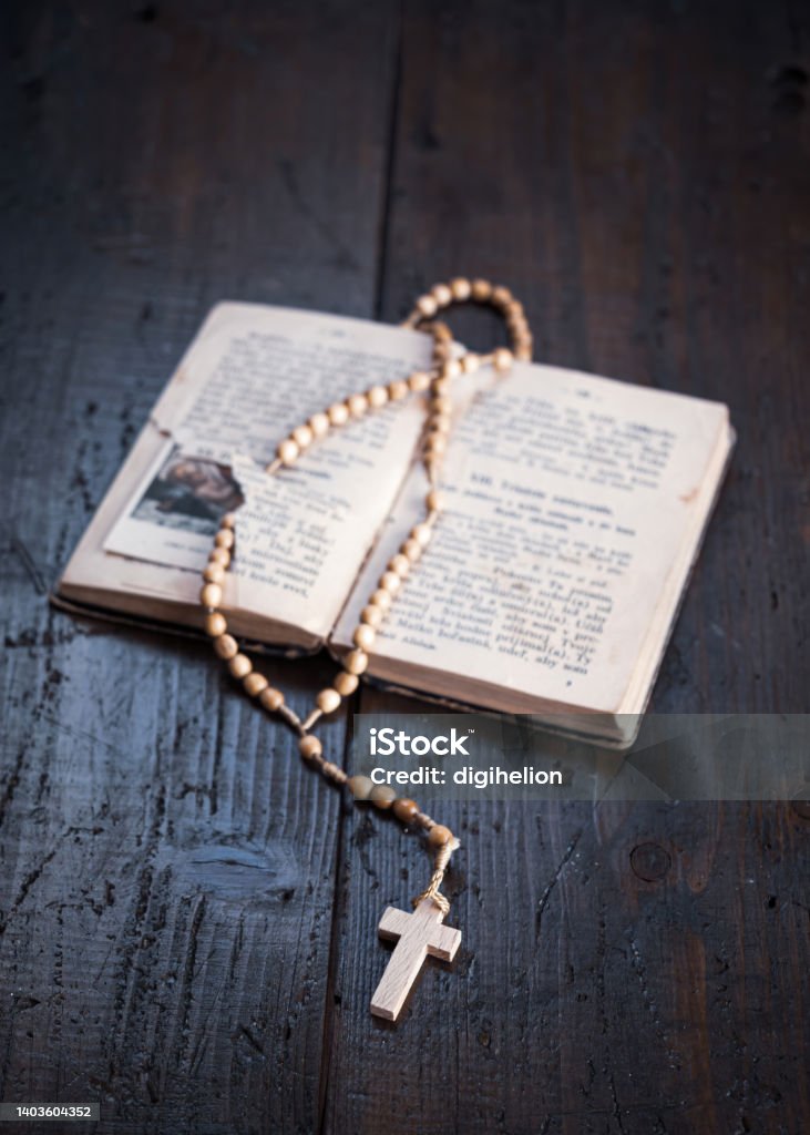 Rosary with cross laying on old open Holy Bible book on wooden table. Rosary with cross laying on old open Holy Bible book on rustic wooden table. Christianity, religion, religious symbol. Prayer. Antique Stock Photo