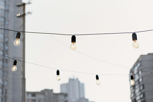 Incandescent light bulbs on wires against city and sky background.