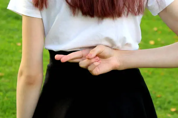 A young girl holds her hands behind her back with her fingers crossed.