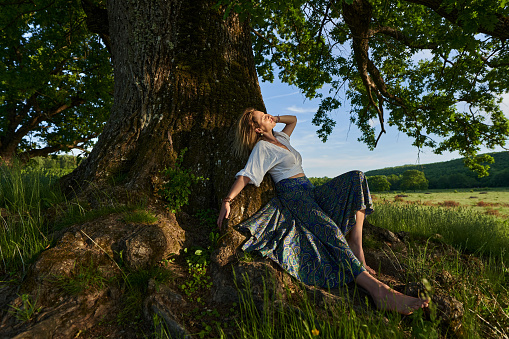 Attractive young blonde woman posing by a huge centennial oak tree at sunset