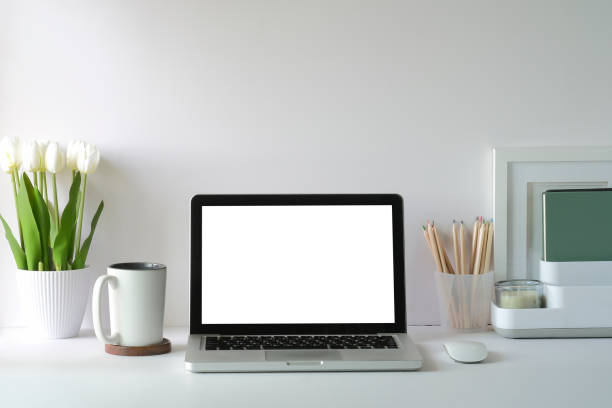 istock Front view laptop computer with blank screen, flower pot, coffee cup and picture frame on white table. 1403609851