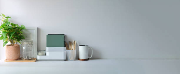 istock Minimal workspace with picture frame, book, coffee cup and pencil holder on white table. Copy space for your advertising text. 1403609854