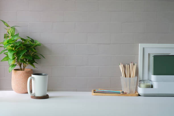 istock Comfortable workplace with picture frame, coffee, stationery and houseplant on white table. Home office, copy space. 1403609856
