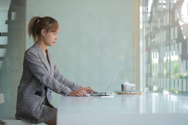istock Young asian female office worker sitting in bright office and working on computer laptop.