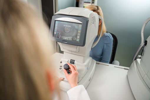 Detail of young optometrist working and controlling optometry device. The screen shows the eye of a Caucasian blond female patient.