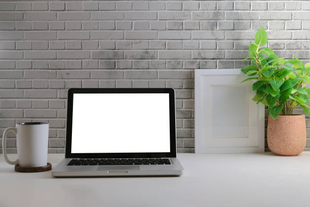 istock Home office desk, laptop computer, coffee cup, potted plant and picture frame on white table with brick wall. 1403611097