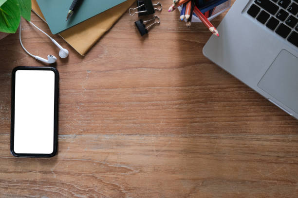 istock Flat lay mockup mobile phone with white screen, laptop computer and supplies on wooden table. 1403611183