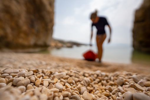 Athletic middle age woman pulling kayak on land, focus on small stones of the beach in foreground, person and rest of the picture blurred, sporty vacations in croatia