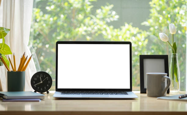 istock Laptop computer with blank display, coffee cup, pencil holder and picture frame on wooden table in bright living room. 1403612871