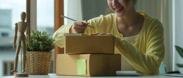 istock Female online store seller writing address on cardboard box while preparing parcel box of product for deliver to customer. 1403615140