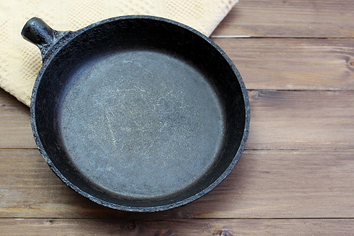 An iron small frying pan stands on a wooden table.