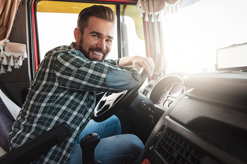 Portrait of young and happy smiling truck driver inside his vehicle