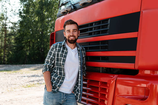 jeune chauffeur de camion souriant à côté de son camion de fret rouge - semi truck truck red truck driver photos et images de collection