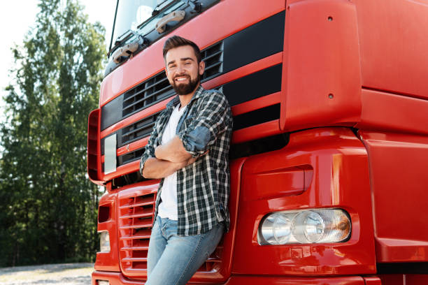 Young smiling male truck driver beside his red cargo truck stock photo