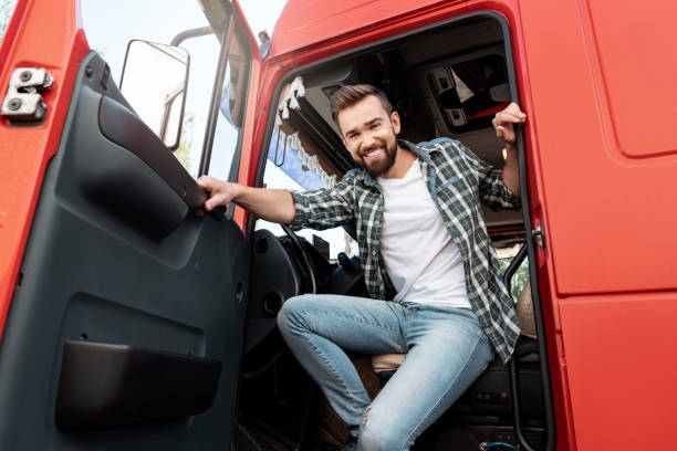 jeune chauffeur de camion souriant à l’intérieur de son camion de fret rouge - semi truck truck red truck driver photos et images de collection