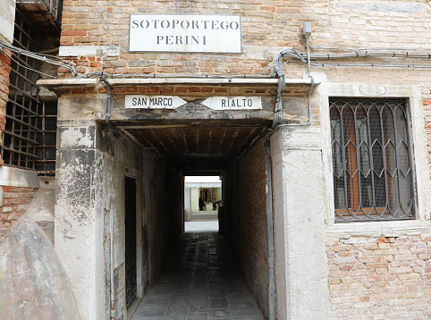Narrow street of Venice in Italy and the text that means Under the Porch called PERINI and the indication to Saint Mark Square or Rialto Bridge in Italian Language