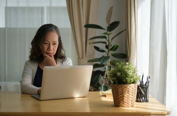 istock Senior mature woman is watching business training, online webinar on laptop computer while remote working from home. 1403620081