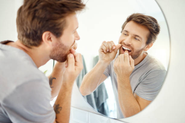 istock One handsome man flossing his teeth in a bathroom at home. Caucasian male using floss to prevent cavities while looking in a mirror in his apartment 1403621337