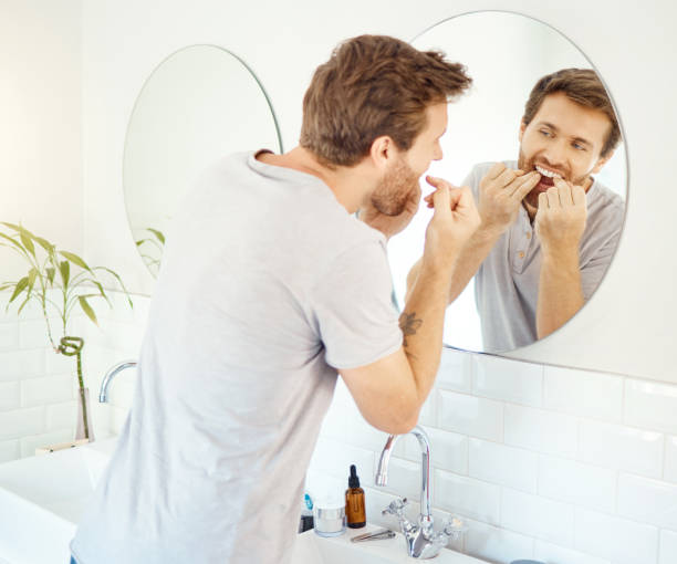 istock One handsome man flossing his teeth in a bathroom at home. Caucasian male using floss to prevent cavities while looking in a mirror in his apartment 1403621342