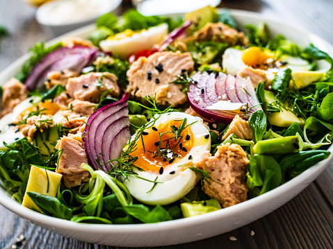 Tuna, boiled eggs, avocado and vegetable salad  on wooden background