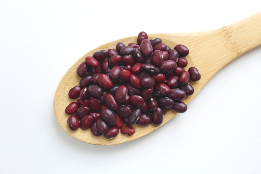 red beans lie on a wooden spoon on a white background.