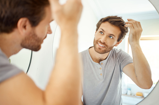 One handsome man combing his hair in a bathroom at home. Caucasian male using a comb to style his hair in the mirror in his apartment.