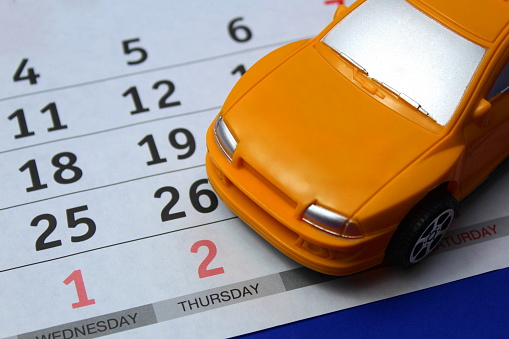A yellow toy car stands against the background of a calendar.