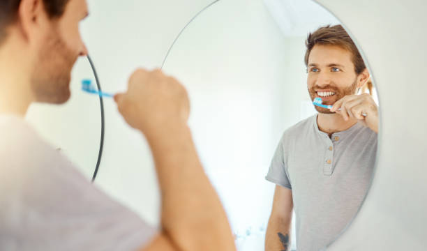 istock One handsome man brushing his teeth in a bathroom at home. Caucasian male using whitening toothpaste and looking in a mirror in his apartment. 1403622773