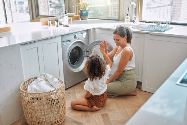 istock Young hispanic mother and her daughter giving each other a high five after doing laundry at home. Adorable little girl helping her mother with household chores 1403623716