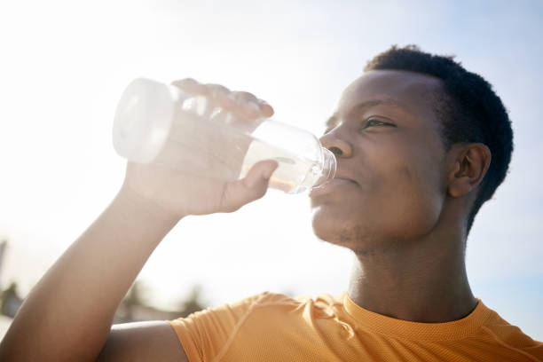 햇빛 아래에서 물 한 병을 마시는 조깅하는 사람. 운동 후 갈증을 해소하는 활동적이고 건강한 아프리카 계 미국인 남자 - drinking water drink men 뉴스 사진 이미지